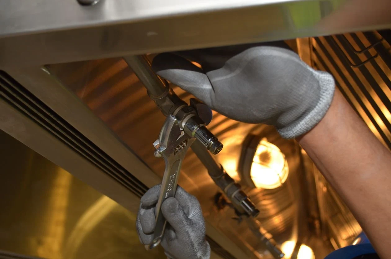Technician checking a pipe fitting with a wrench during a water heater leak inspection